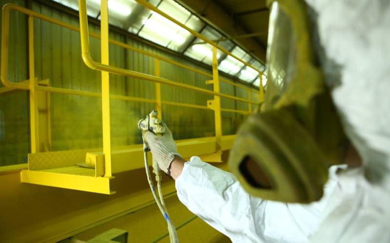 A painter paints an iron catwalk in an industrial factory.