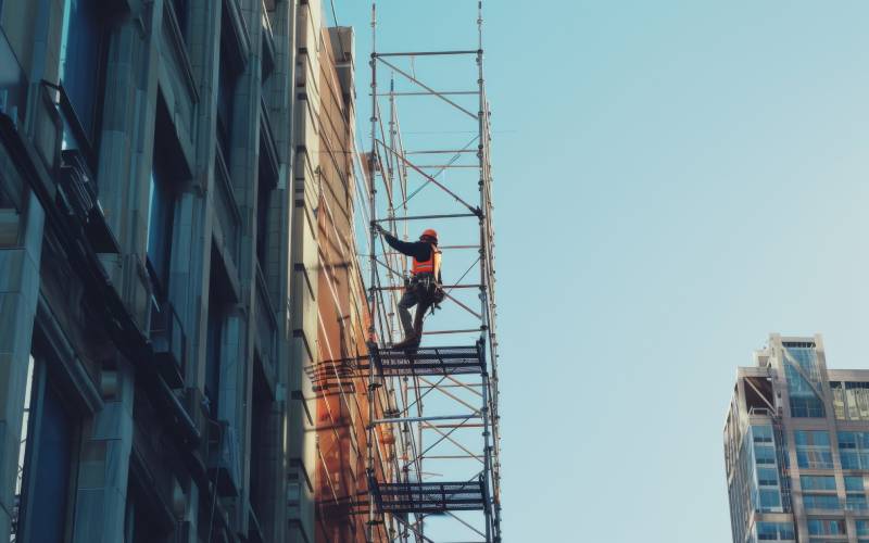 Construction worker performing building maintenance while standing on scaffolding